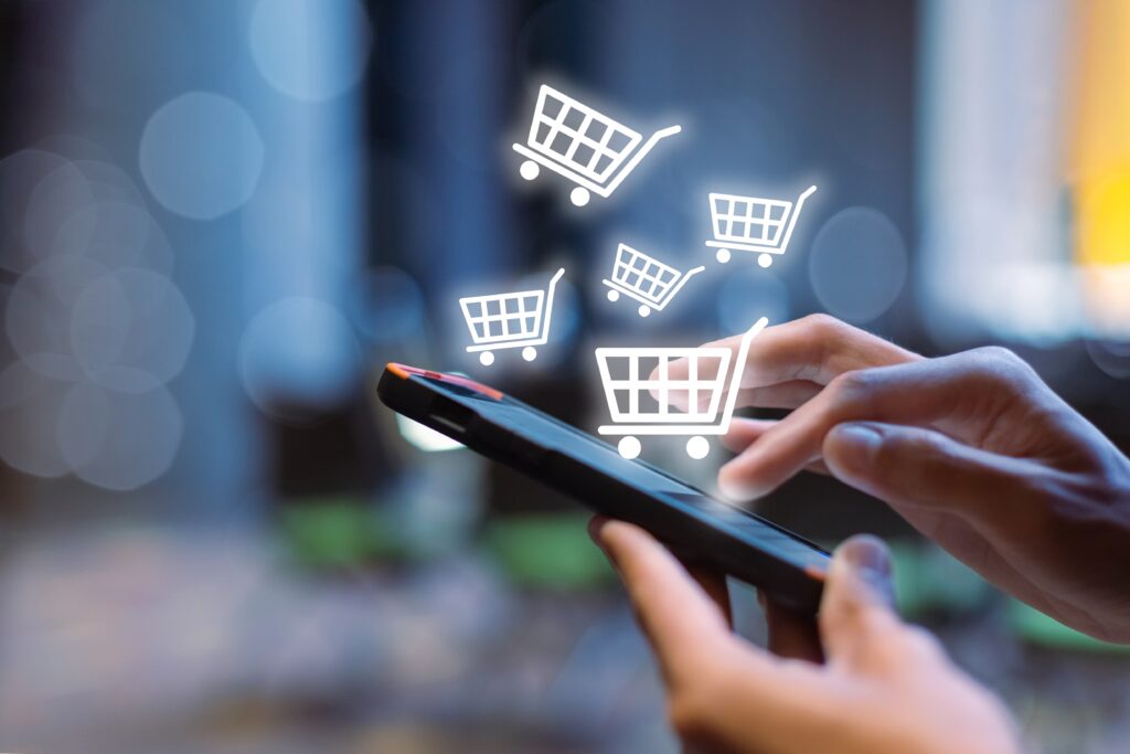 Smartphone in hand with shopping cart icons rising from the screen